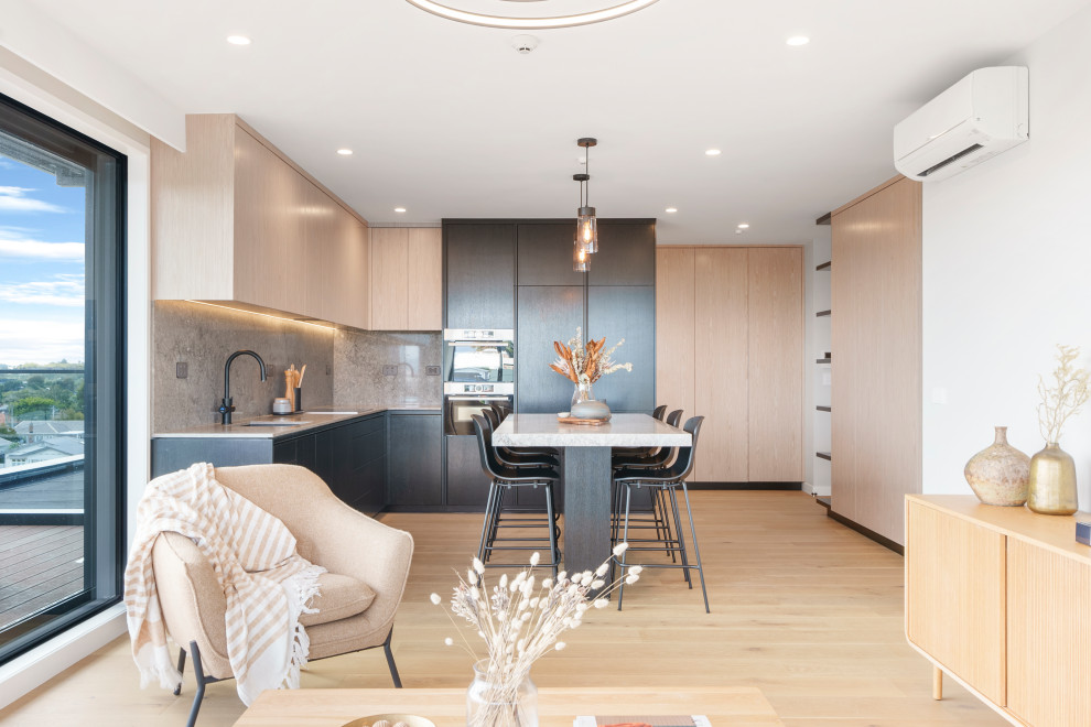 Immagine di un cucina con isola centrale design con ante in legno chiaro, paraspruzzi grigio, elettrodomestici neri e top grigio