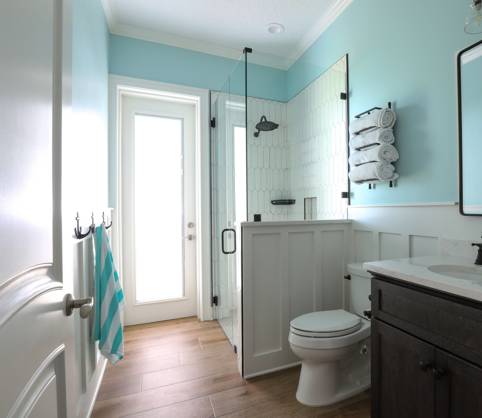Photo of a mid-sized beach style kids bathroom in Jacksonville with flat-panel cabinets, brown cabinets, a curbless shower, a two-piece toilet, white tile, ceramic tile, blue walls, porcelain floors, an undermount sink, engineered quartz benchtops, brown floor, a hinged shower door, white benchtops, a single vanity, a built-in vanity and decorative wall panelling.