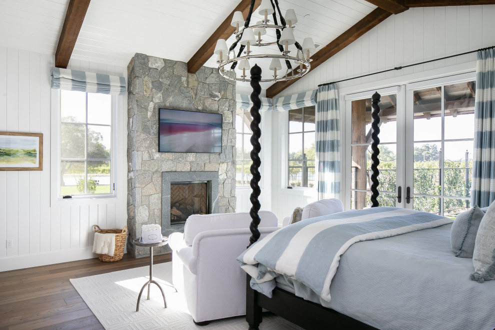 Design ideas for a country bedroom in Orange County with white walls, dark hardwood floors, a standard fireplace, a stone fireplace surround, brown floor, exposed beam, timber, vaulted and planked wall panelling.