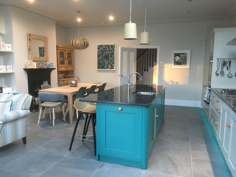 Photo of a mid-sized traditional single-wall open plan kitchen in London with a farmhouse sink, shaker cabinets, turquoise cabinets, quartzite benchtops, stainless steel appliances, porcelain floors, with island, grey floor, black benchtop, black splashback and stone slab splashback.