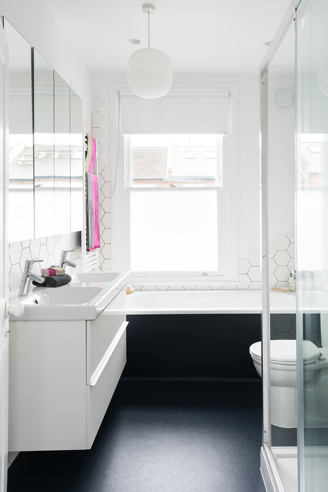 Photo of a contemporary 3/4 bathroom in London with flat-panel cabinets, white cabinets, an alcove tub, a two-piece toilet, white tile, white walls, a console sink, black floor and a sliding shower screen.