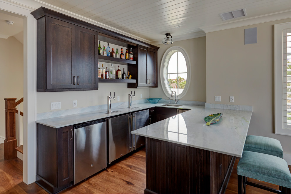 This is an example of a mid-sized beach style u-shaped seated home bar in Jacksonville with an undermount sink, shaker cabinets, brown cabinets, quartzite benchtops, blue splashback, stone slab splashback, medium hardwood floors and brown floor.