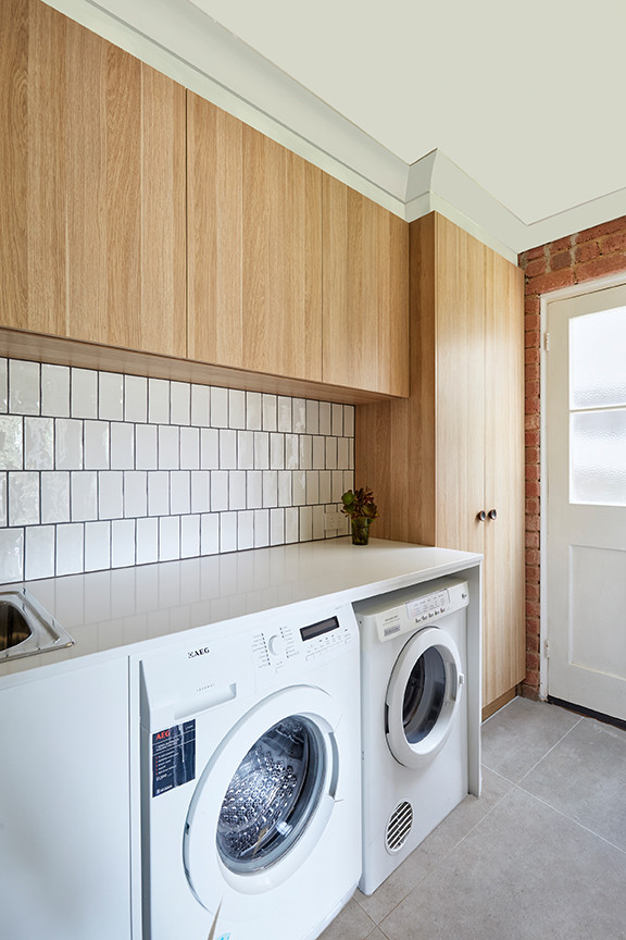 Mid-sized contemporary single-wall dedicated laundry room in Melbourne with a farmhouse sink, raised-panel cabinets, light wood cabinets, solid surface benchtops, slate floors and a side-by-side washer and dryer.
