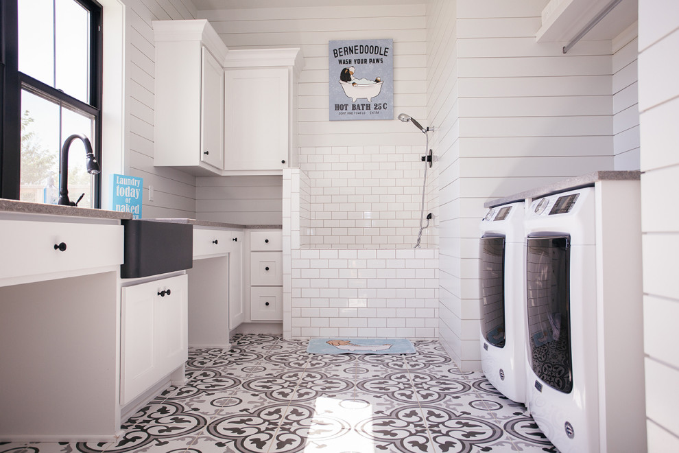 This is an example of a mid-sized country laundry room in Portland with a drop-in sink, white cabinets, window splashback, white walls, a side-by-side washer and dryer, multi-coloured floor and grey benchtop.