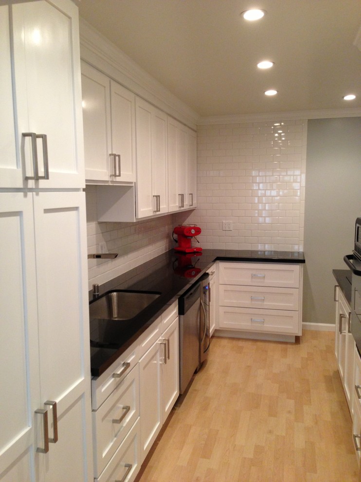 This is an example of a small transitional galley separate kitchen in Los Angeles with an undermount sink, recessed-panel cabinets, white cabinets, solid surface benchtops, white splashback, subway tile splashback, stainless steel appliances, light hardwood floors and no island.