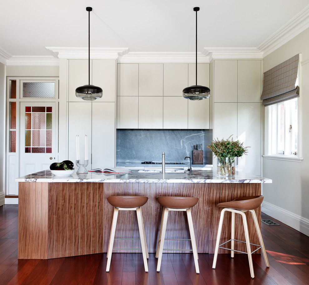 Eclectic galley eat-in kitchen in Sydney with an undermount sink, flat-panel cabinets, marble benchtops, grey splashback, stone slab splashback, stainless steel appliances, medium hardwood floors, with island, brown floor, multi-coloured benchtop and beige cabinets.