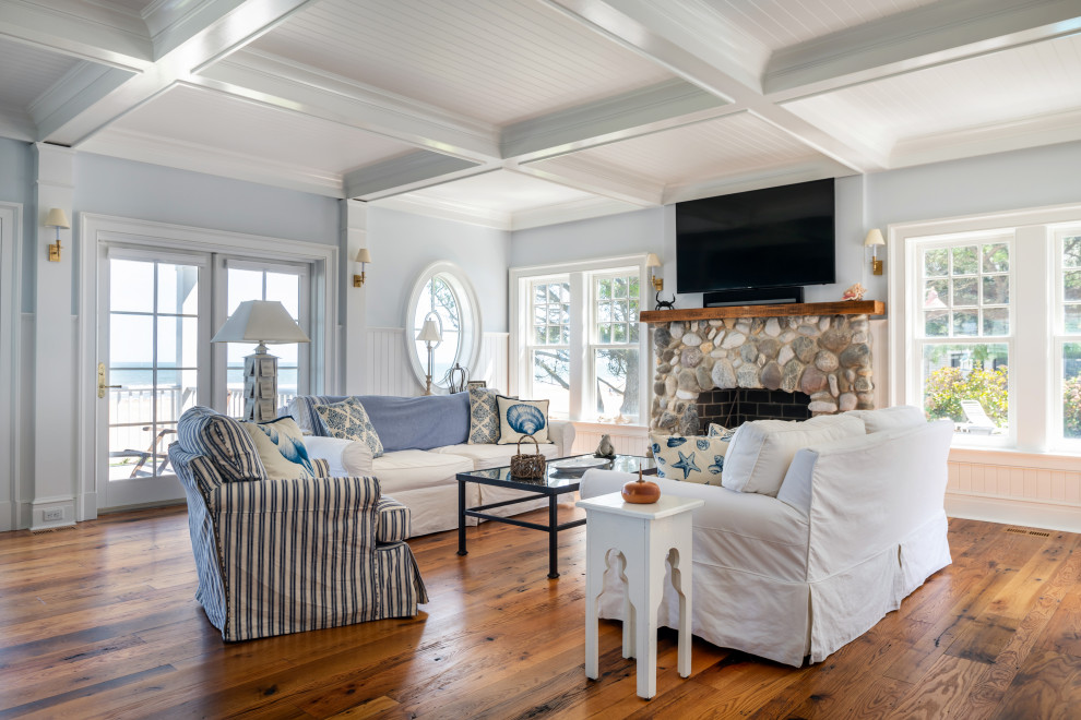 This is an example of a large beach style open concept living room in Other with a stone fireplace surround, grey walls, medium hardwood floors, a standard fireplace, a wall-mounted tv, brown floor, coffered and decorative wall panelling.