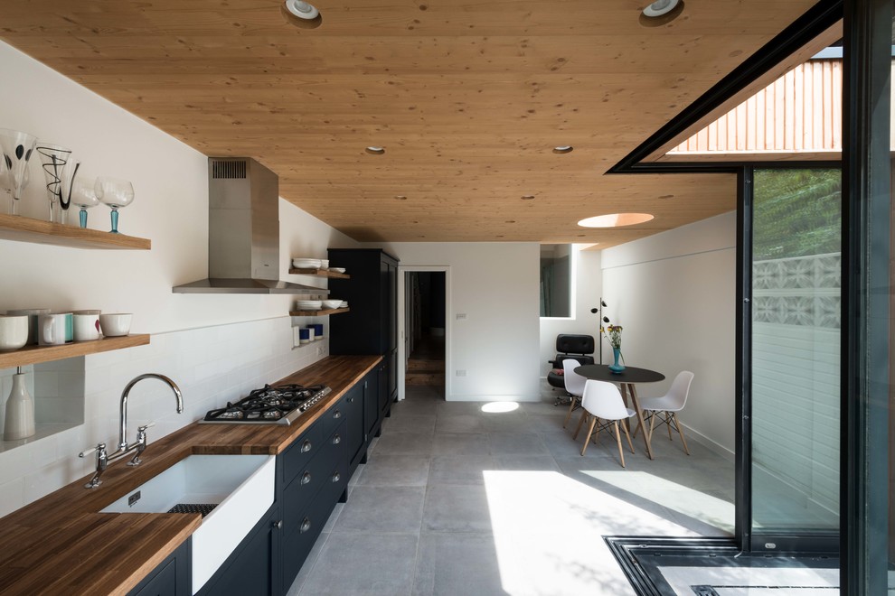 Design ideas for a mid-sized contemporary single-wall eat-in kitchen in Oxfordshire with shaker cabinets, wood benchtops, white splashback, no island, grey floor, brown benchtop, a farmhouse sink and black cabinets.