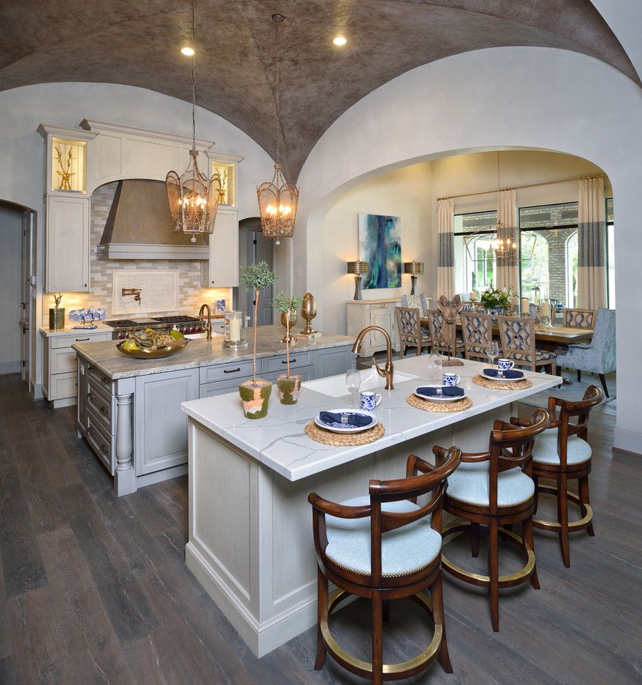 Large eclectic l-shaped open plan kitchen in Houston with a farmhouse sink, recessed-panel cabinets, white cabinets, quartzite benchtops, beige splashback, subway tile splashback, stainless steel appliances, dark hardwood floors, multiple islands and grey floor.
