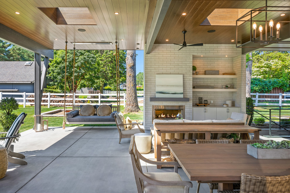 Immagine di un ampio patio o portico classico dietro casa con un caminetto, lastre di cemento e un tetto a sbalzo