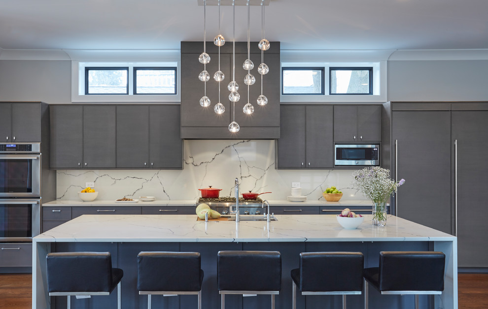 This is an example of a large contemporary single-wall open plan kitchen in Chicago with an undermount sink, flat-panel cabinets, grey cabinets, quartz benchtops, white splashback, panelled appliances, medium hardwood floors, with island and white benchtop.