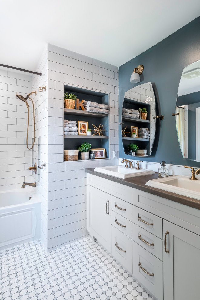 This is an example of a transitional bathroom in Milwaukee with shaker cabinets, grey cabinets, an alcove tub, a shower/bathtub combo, white tile, grey walls, mosaic tile floors, a drop-in sink, multi-coloured floor, a shower curtain, brown benchtops, a double vanity and a freestanding vanity.