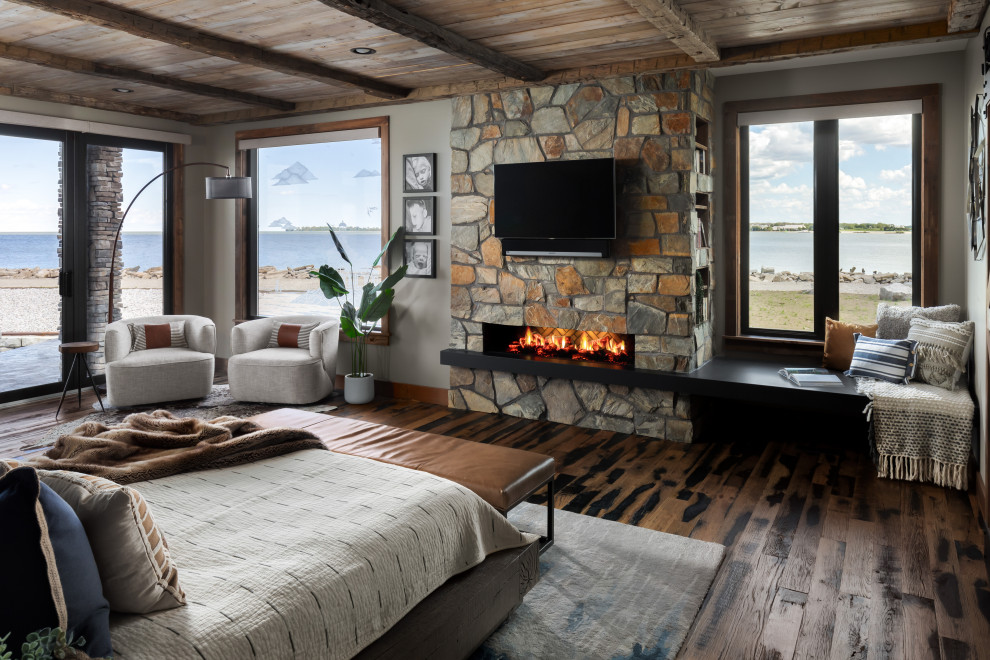 Cette image montre une chambre parentale rustique de taille moyenne avec un mur gris, un sol en bois brun, une cheminée standard, un manteau de cheminée en pierre, un sol marron et un plafond en lambris de bois.