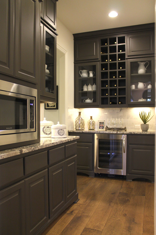 This is an example of a large traditional l-shaped kitchen pantry in Austin with raised-panel cabinets, grey cabinets, granite benchtops, multi-coloured splashback, subway tile splashback, stainless steel appliances and medium hardwood floors.