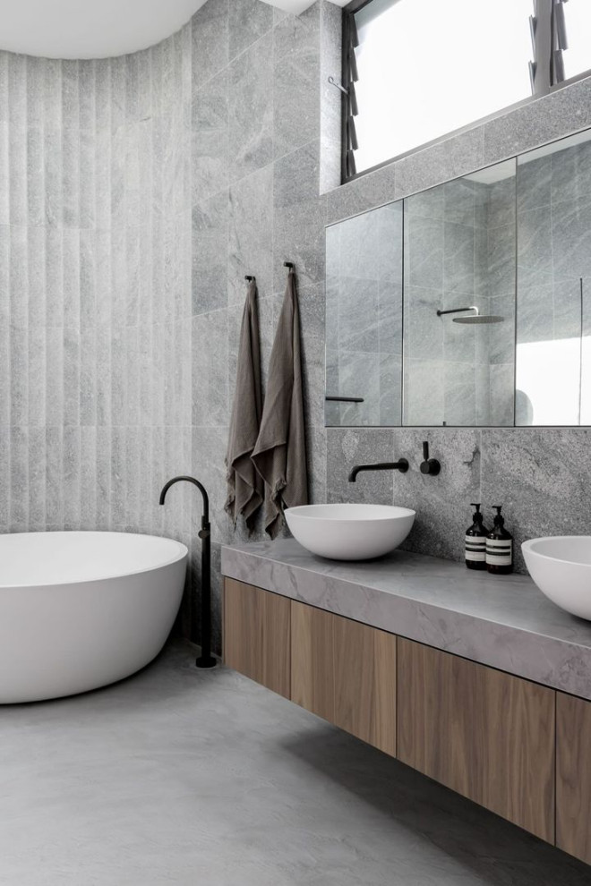 Photo of a large contemporary master bathroom in Other with medium wood cabinets, a freestanding tub, gray tile, grey walls, concrete floors, a vessel sink, grey floor, grey benchtops, a double vanity and a floating vanity.
