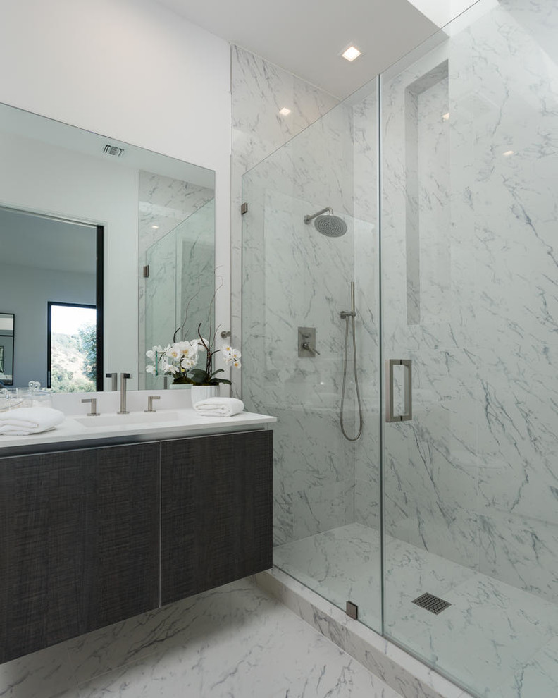 Inspiration for a large contemporary master bathroom in Los Angeles with flat-panel cabinets, dark wood cabinets, a freestanding tub, a curbless shower, white tile, stone slab, white walls, marble floors, marble benchtops, an integrated sink and a hinged shower door.