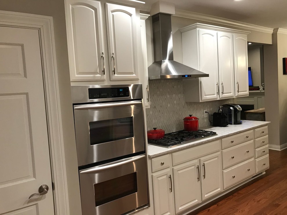 Mid-sized traditional galley kitchen in Columbus with an undermount sink, raised-panel cabinets, white cabinets, quartzite benchtops, white splashback, glass tile splashback, panelled appliances, dark hardwood floors, a peninsula, brown floor and white benchtop.
