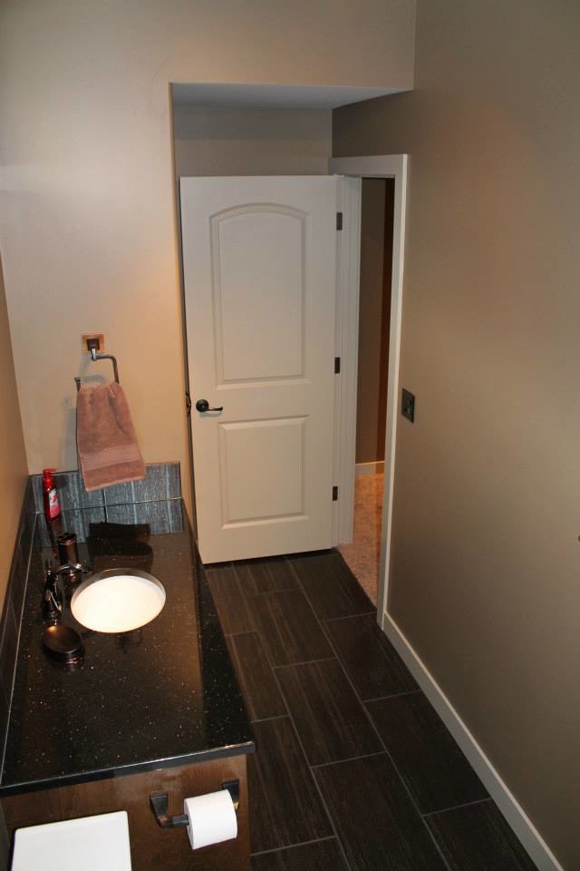 Small transitional 3/4 brown tile and stone tile vinyl floor alcove shower photo with recessed-panel cabinets, dark wood cabinets, a two-piece toilet, brown walls, an undermount sink and granite countertops