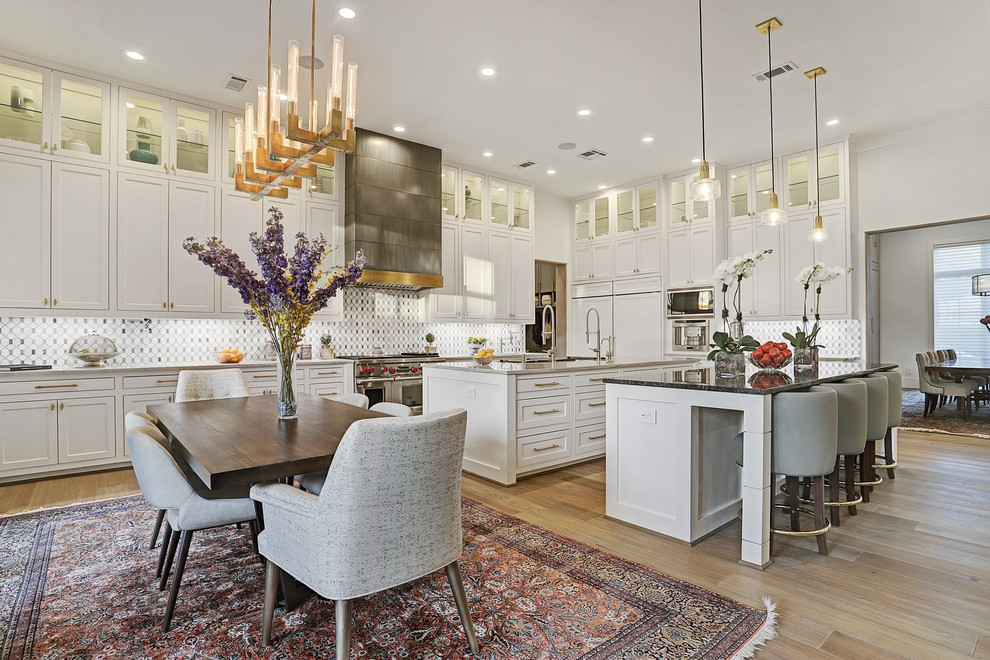 Photo of an expansive transitional l-shaped eat-in kitchen in Houston with recessed-panel cabinets, white cabinets, quartz benchtops, white splashback, marble splashback, stainless steel appliances, multiple islands, grey benchtop, medium hardwood floors and brown floor.