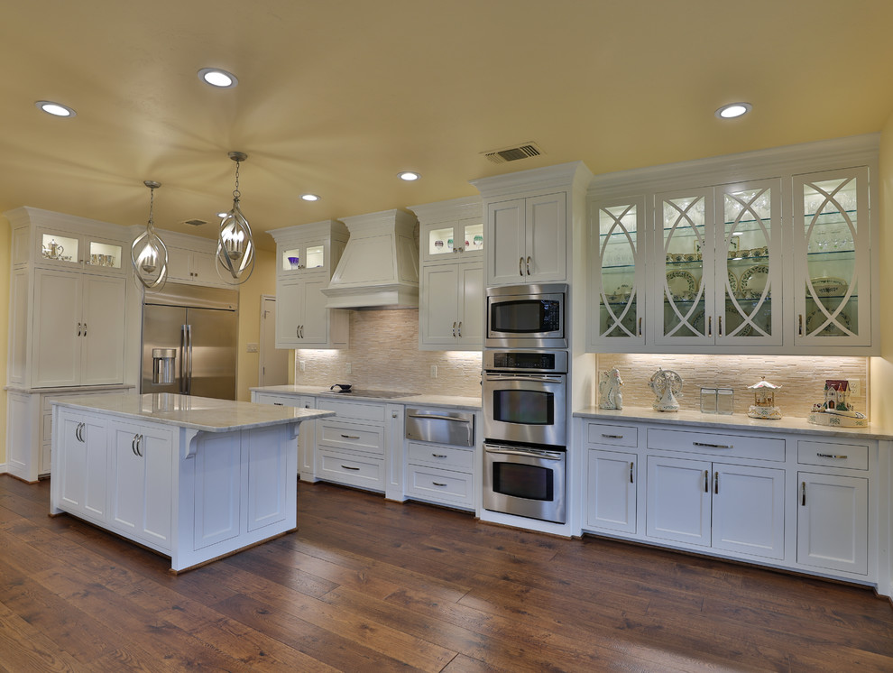 Inspiration for a transitional kitchen in Dallas with an undermount sink, recessed-panel cabinets, white cabinets, quartzite benchtops, beige splashback, stone tile splashback, stainless steel appliances, dark hardwood floors, with island, brown floor and beige benchtop.