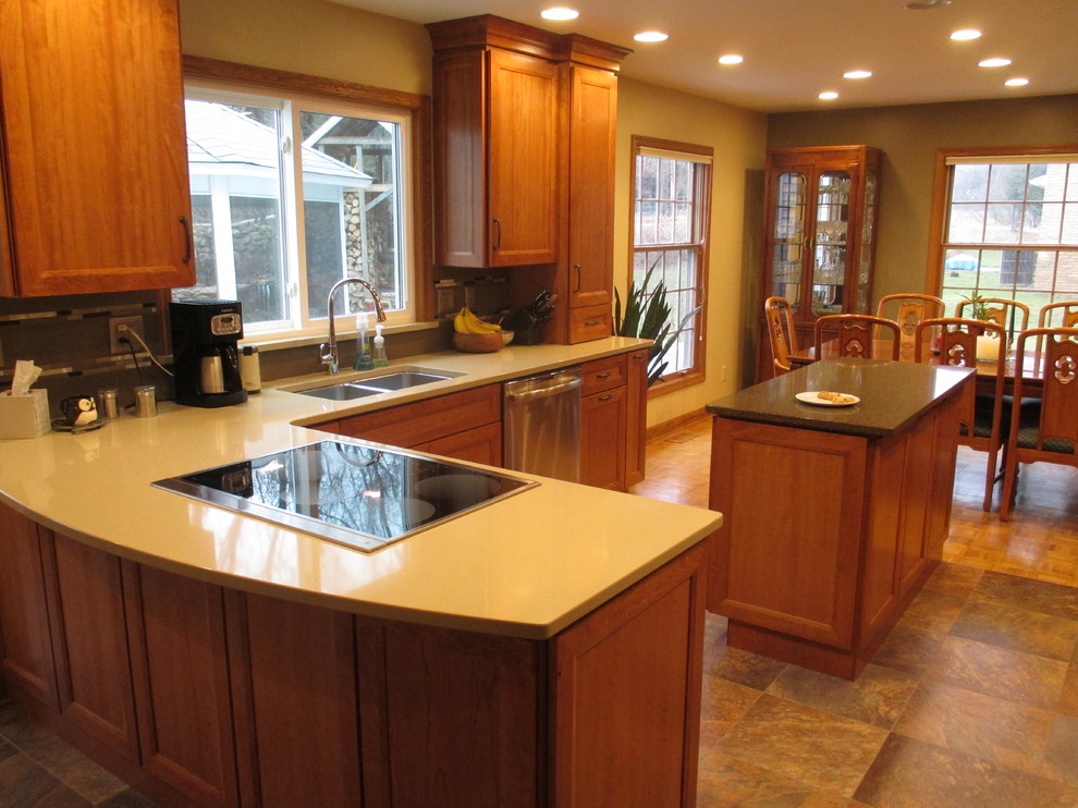 Example of a mid-sized transitional u-shaped slate floor eat-in kitchen design with an undermount sink, recessed-panel cabinets, medium tone wood cabinets, solid surface countertops, stainless steel appliances and a peninsula