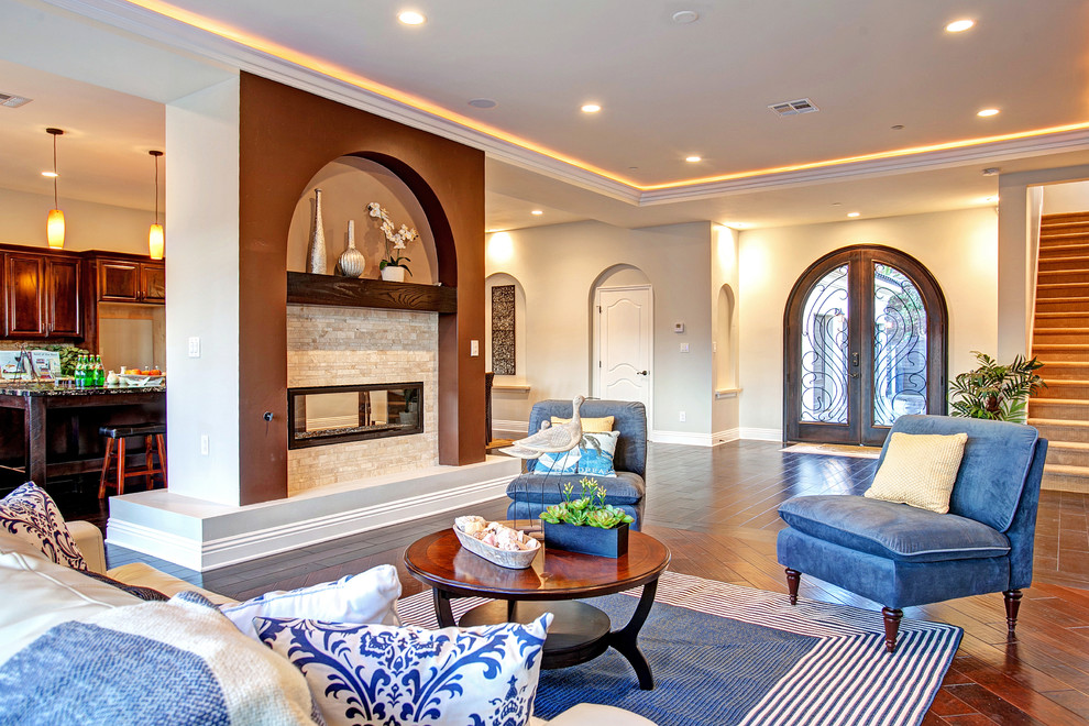 Photo of a large traditional formal open concept living room in Orange County with beige walls, dark hardwood floors, a two-sided fireplace, a stone fireplace surround and a wall-mounted tv.