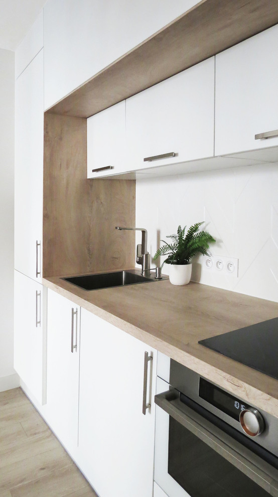 This is an example of a mid-sized modern single-wall open plan kitchen in Paris with a single-bowl sink, flat-panel cabinets, white cabinets, laminate benchtops, white splashback, ceramic splashback, white appliances, light hardwood floors, no island, beige floor and beige benchtop.