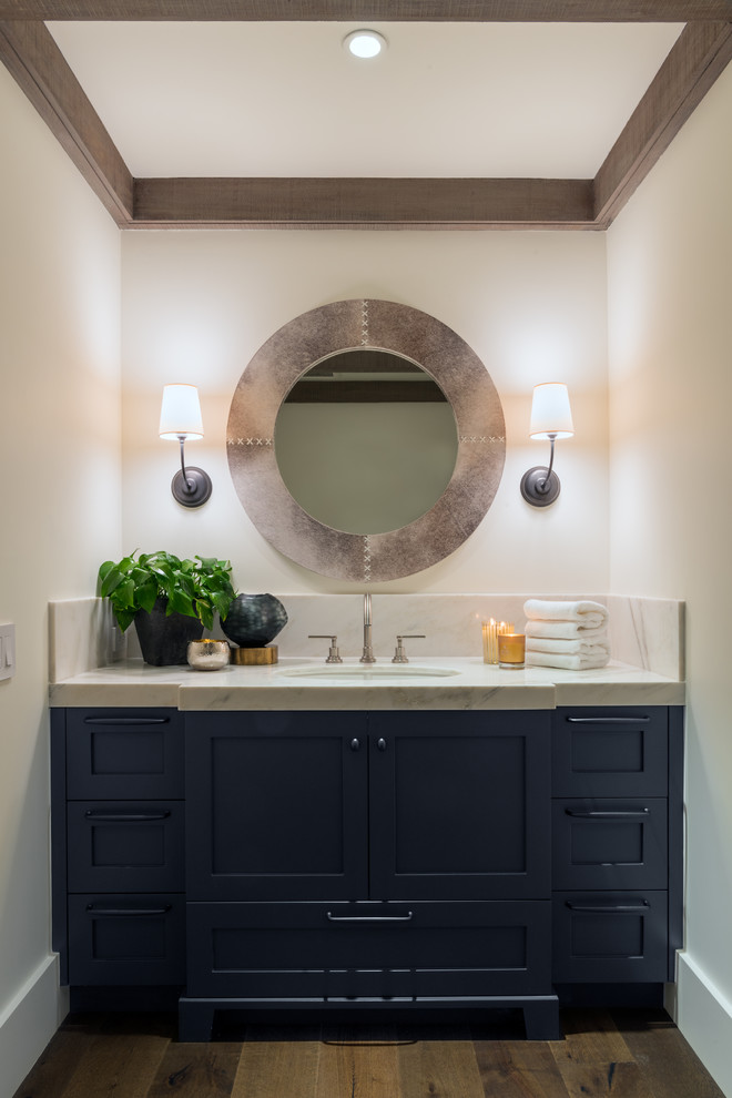 This is an example of a small country powder room in San Francisco with shaker cabinets, blue cabinets, stone slab, white walls, dark hardwood floors, an undermount sink and marble benchtops.