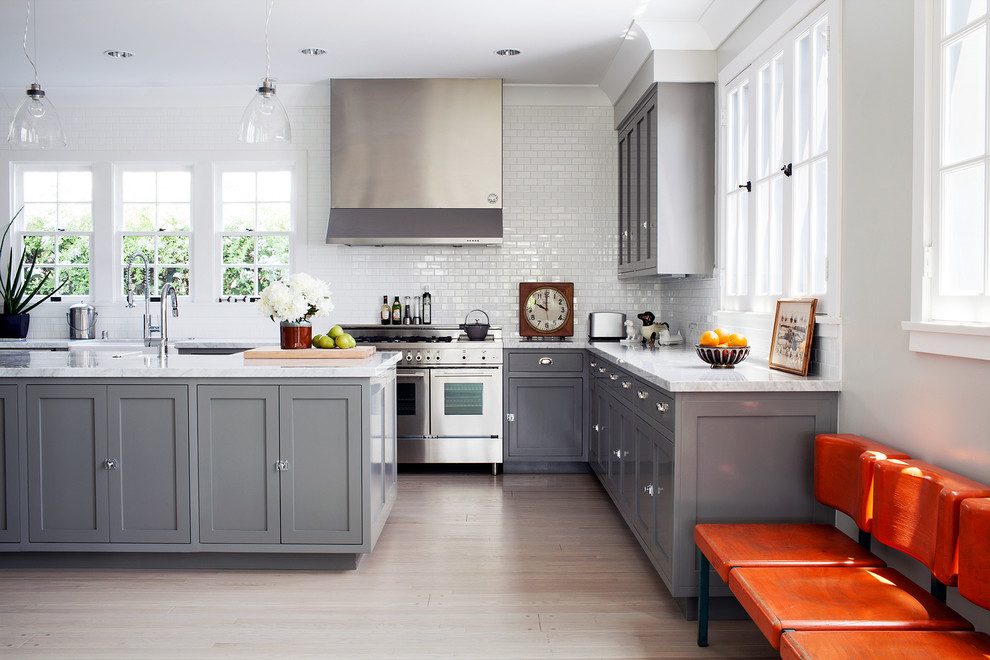 Photo of a transitional l-shaped kitchen in Los Angeles with shaker cabinets, grey cabinets, white splashback, subway tile splashback, stainless steel appliances, light hardwood floors and with island.