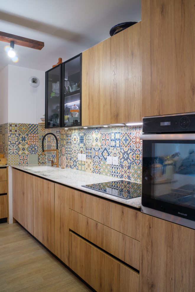 This is an example of a mid-sized modern l-shaped open plan kitchen in Paris with an integrated sink, beaded inset cabinets, medium wood cabinets, cement tile splashback, panelled appliances, laminate floors and white benchtop.