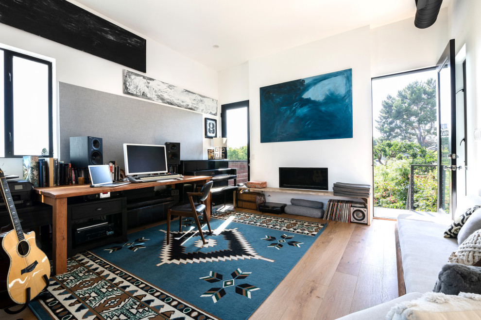 Mid-sized contemporary home studio in Los Angeles with multi-coloured walls, medium hardwood floors, a standard fireplace, a metal fireplace surround, a freestanding desk and brown floor.