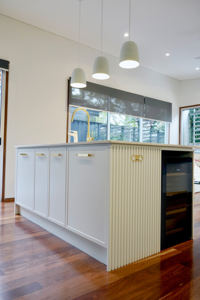 Large modern l-shaped open plan kitchen in Sydney with an undermount sink, shaker cabinets, turquoise cabinets, marble benchtops, white splashback, matchstick tile splashback, black appliances, dark hardwood floors, with island, brown floor and white benchtop.