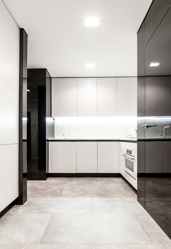 Inspiration for a mid-sized contemporary l-shaped open plan kitchen in Other with an undermount sink, flat-panel cabinets, solid surface benchtops, porcelain splashback, white appliances, porcelain floors, grey floor, white benchtop, white splashback and no island.