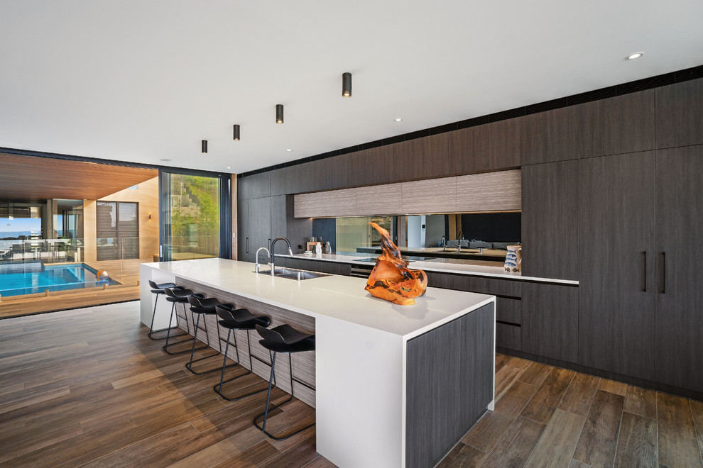 Design ideas for an expansive contemporary galley open plan kitchen in Central Coast with flat-panel cabinets, dark wood cabinets, solid surface benchtops, black splashback, mirror splashback, black appliances, with island and white benchtop.
