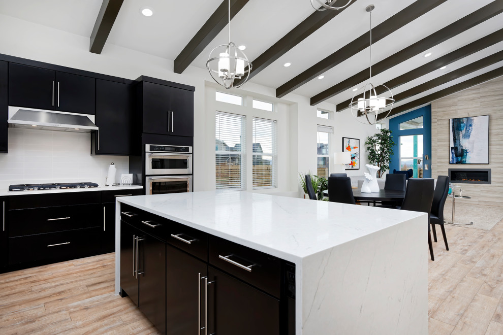 Große Mid-Century Wohnküche in U-Form mit schwarzen Schränken, Quarzwerkstein-Arbeitsplatte, Küchenrückwand in Weiß, Küchengeräten aus Edelstahl, Kücheninsel, braunem Boden, weißer Arbeitsplatte und freigelegten Dachbalken in Denver