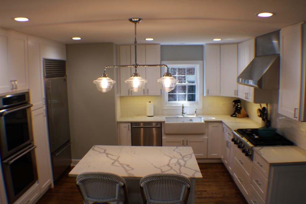 Design ideas for a mid-sized contemporary l-shaped open plan kitchen in Chicago with a farmhouse sink, shaker cabinets, white cabinets, marble benchtops, white splashback, subway tile splashback, stainless steel appliances, medium hardwood floors, with island and brown floor.