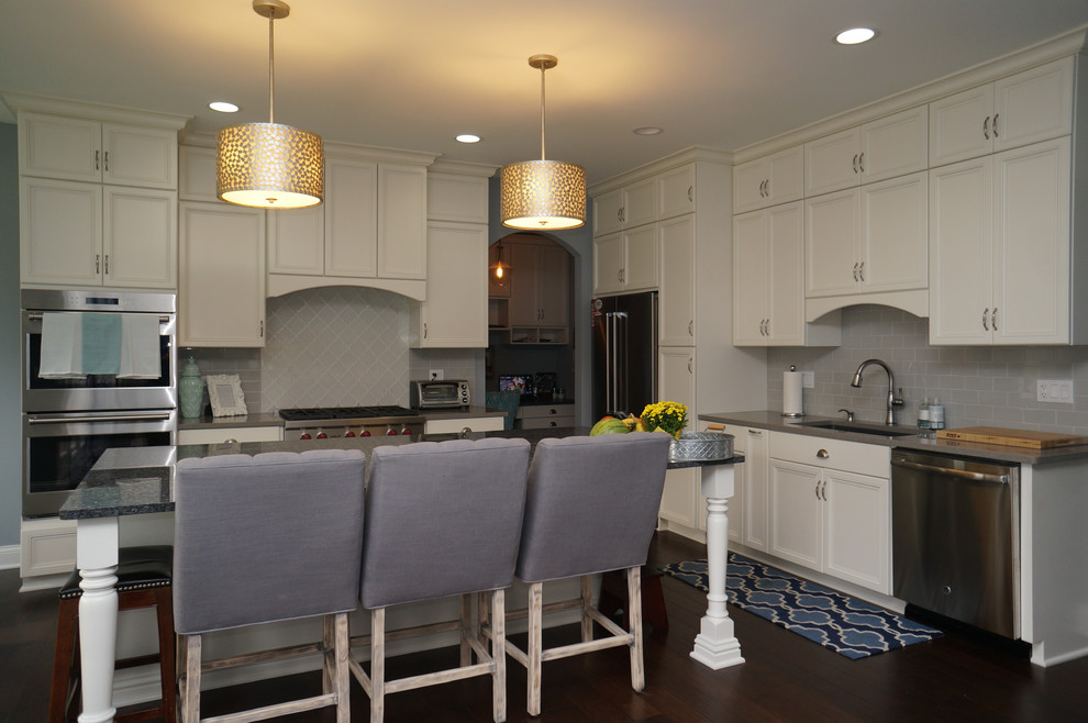 This is an example of a large traditional l-shaped kitchen in Chicago with a drop-in sink, white cabinets, granite benchtops, grey splashback, ceramic splashback, stainless steel appliances, dark hardwood floors and with island.