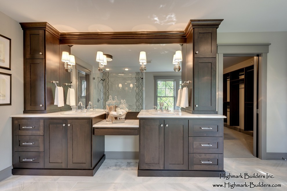 This is an example of a traditional master bathroom in Minneapolis with a drop-in sink, furniture-like cabinets, dark wood cabinets, marble benchtops, a freestanding tub, a two-piece toilet, beige tile, porcelain tile, beige walls and marble floors.