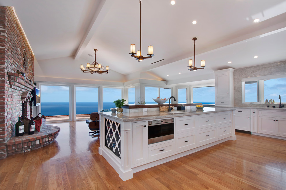 This is an example of an expansive arts and crafts l-shaped eat-in kitchen in Los Angeles with an undermount sink, shaker cabinets, white cabinets, quartzite benchtops, white splashback, stone slab splashback, stainless steel appliances, light hardwood floors, with island and beige floor.