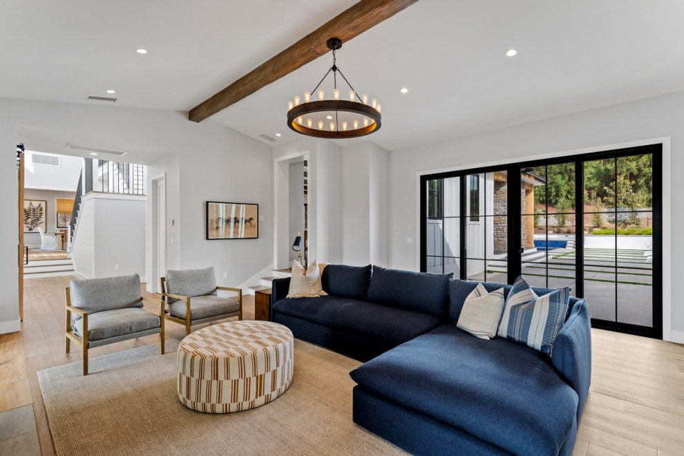 Example of a huge country open concept light wood floor, beige floor and exposed beam living room design in Los Angeles with white walls, a standard fireplace, a stone fireplace and a wall-mounted tv