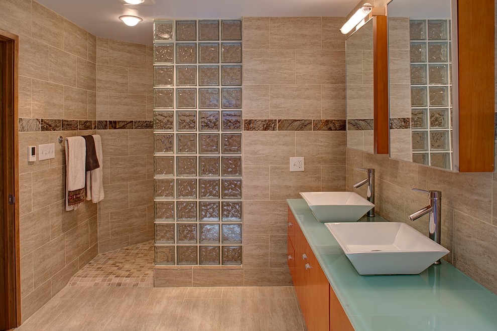 Mid-sized modern master bathroom in Baltimore with flat-panel cabinets, medium wood cabinets, a drop-in tub, beige tile, beige walls, limestone floors, a vessel sink, glass benchtops and limestone.