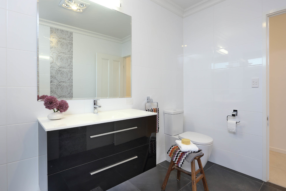 Design ideas for a mid-sized modern bathroom in Brisbane with an integrated sink, flat-panel cabinets, solid surface benchtops, a one-piece toilet, white tile, ceramic tile, white walls, porcelain floors and black cabinets.