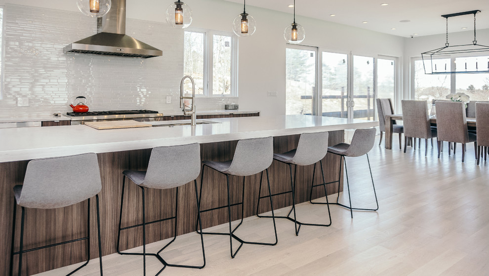 Design ideas for a large contemporary l-shaped eat-in kitchen in Boston with with island, an undermount sink, flat-panel cabinets, medium wood cabinets, quartz benchtops, white splashback, glass tile splashback, stainless steel appliances, light hardwood floors and white floor.