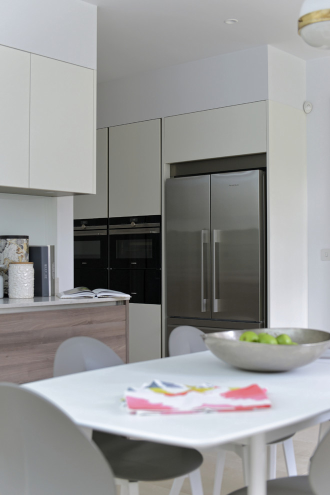 Inspiration for a large contemporary l-shaped eat-in kitchen in Gloucestershire with an undermount sink, flat-panel cabinets, white cabinets, solid surface benchtops, green splashback, glass sheet splashback, stainless steel appliances, porcelain floors and no island.