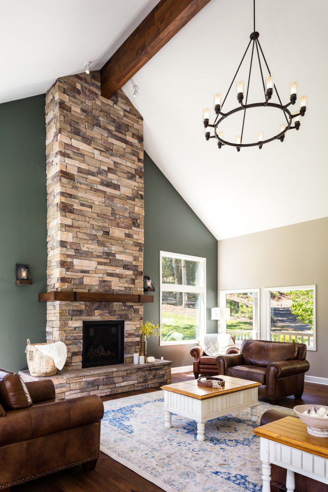Exemple d'un salon montagne ouvert avec un mur vert, un sol en bois brun, une cheminée standard, aucun téléviseur, un sol marron, poutres apparentes et un manteau de cheminée en pierre de parement.