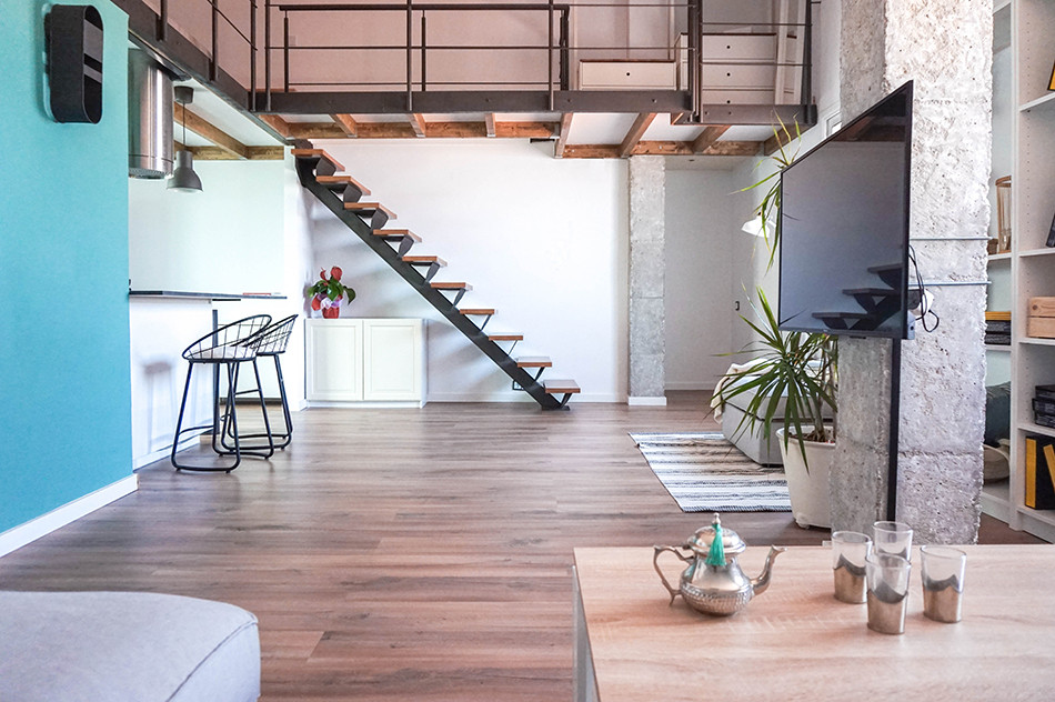 Ejemplo de sala de estar tipo loft industrial de tamaño medio sin chimenea con paredes blancas, suelo laminado, televisor en una esquina y suelo marrón