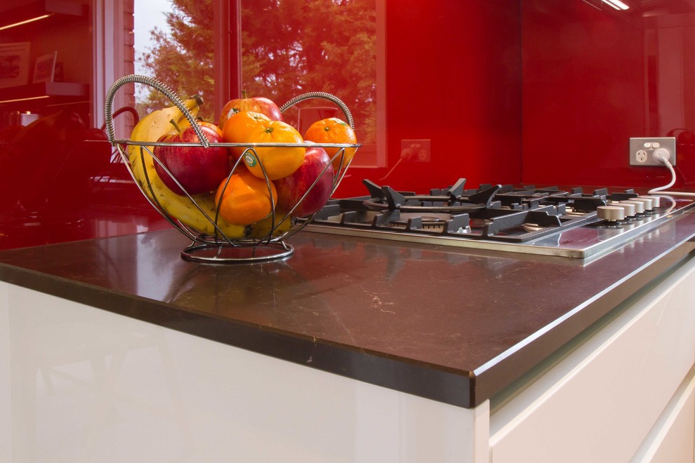 Photo of a mid-sized contemporary u-shaped eat-in kitchen in Melbourne with flat-panel cabinets, quartz benchtops, red splashback, glass sheet splashback, medium hardwood floors and a peninsula.