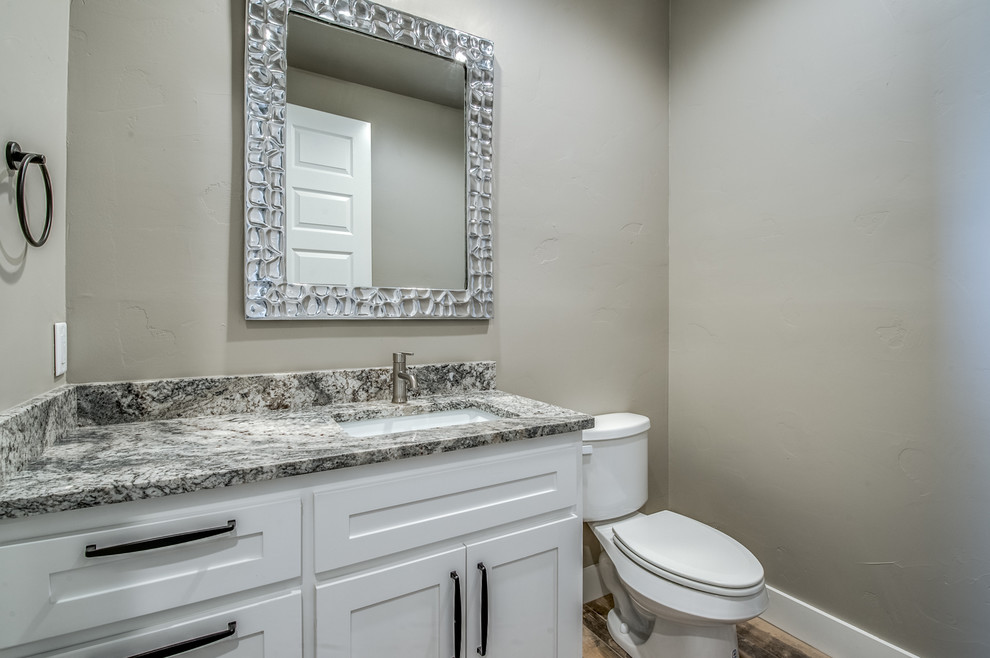 This is an example of a mid-sized transitional powder room in Austin with shaker cabinets, white cabinets, a two-piece toilet, grey walls, porcelain floors, an undermount sink, granite benchtops, beige floor and grey benchtops.
