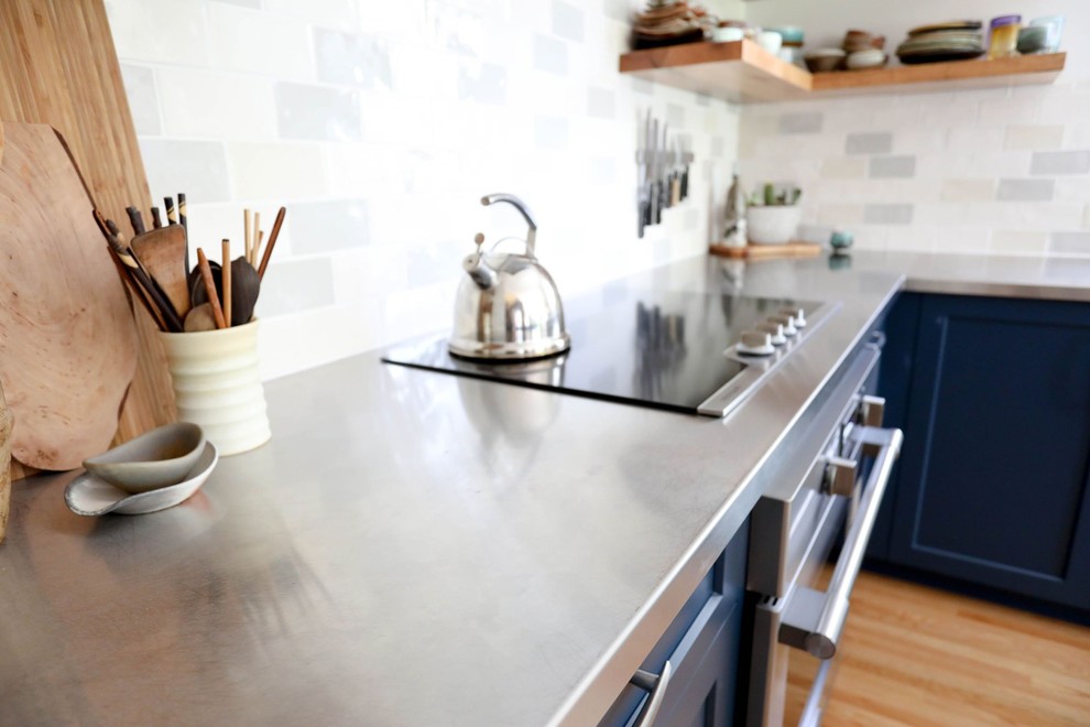 Open concept kitchen - mid-sized transitional l-shaped light wood floor and beige floor open concept kitchen idea with an integrated sink, shaker cabinets, blue cabinets, stainless steel countertops, ceramic backsplash, stainless steel appliances, an island and gray countertops