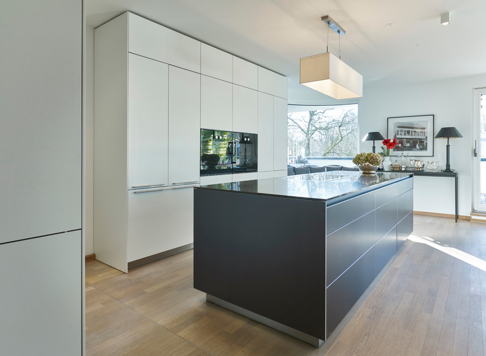 This is an example of a large contemporary galley open plan kitchen in Munich with flat-panel cabinets, white cabinets, light hardwood floors, with island and panelled appliances.